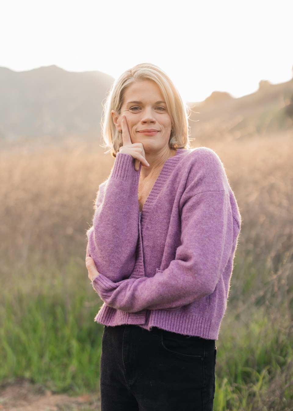Caileen Kehayas Holden with a thoughtful smile, hand on chin, in a golden field