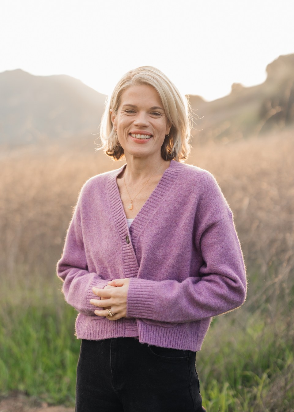 Caileen Kehayas Holden smiling in a lavender cardigan in a golden field
